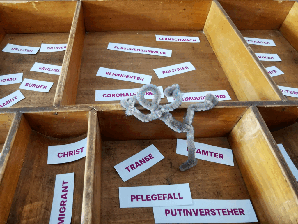 Männchen aus Pfeifenreinigern klettert von einem Schubladenfach in das nächste, umgeben von Schlagworten.